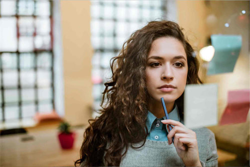 Woman looking at sticky notes thoughtfully, with pen held to her chin