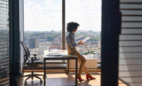 Woman sitting on her desk, looking at papers with a city view in the background