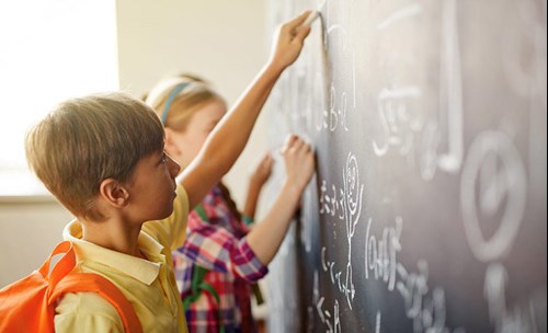 Two children writing on a black board with chalk